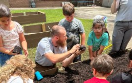 Spencer Barker shows campers how to plant seedlings in their garden