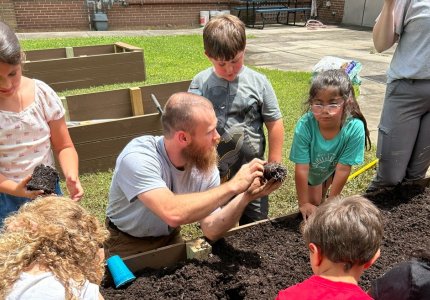 Spencer Barker shows campers how to plant seedlings in their garden