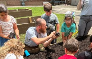 Spencer Barker shows campers how to plant seedlings in their garden