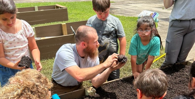Spencer Barker shows campers how to plant seedlings in their garden